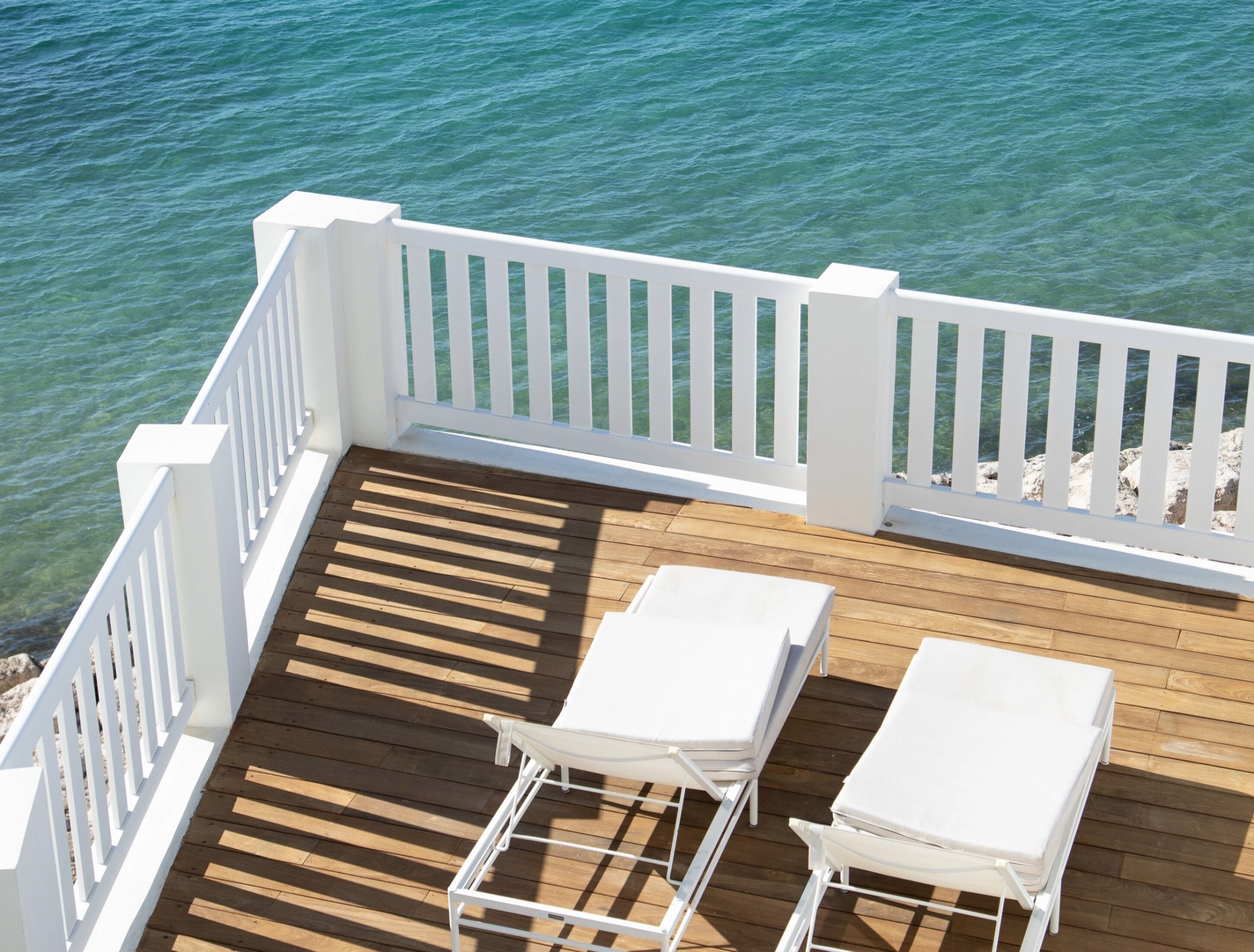 Una terraza de madera con barandillas blancas y dos sillones reclinables blancos.