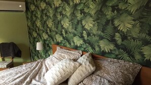 A bed with patterned bedding and two pillows, a wall-mounted lamp, and a chair with a blanket. - Sanddala Bed & Breakfast (Everöd)