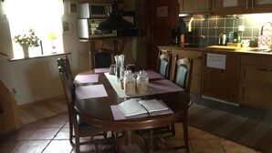 A dining area with a round table, chairs, and a kitchen in the background. - Sanddala Bed & Breakfast (Everöd)