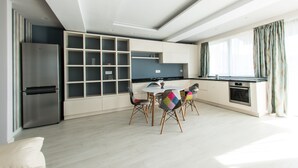 Una cocina moderna con un refrigerador empotrado, un comedor con una mesa redonda y sillas coloridas, y un amplio ventanal con cortinas.