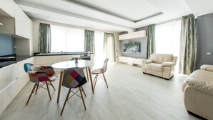 Una sala de estar moderna con una mesa redonda para comer, sillas coloridas, un sofá y un televisor.