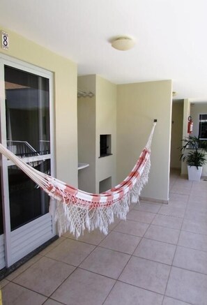 A hammock in a hallway with tiled flooring, a sliding glass door, and a potted plant.