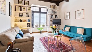 Un salon avec un canapé, une table basse et un téléviseur. On y trouve des étagères avec des photos encadrées et une plante en pot.