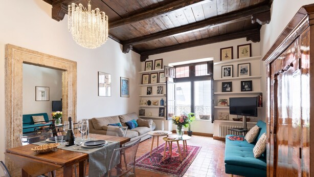Un salon chaleureux avec une table à manger en bois, un canapé et un téléviseur. Les murs sont ornés de tableaux encadrés et un lustre est suspendu au plafond.