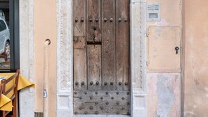 Une grande porte en bois ornée d’un motif métallique décoratif, une petite fenêtre au-dessus et un carillon.