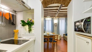 Une cuisine équipée d’une cuisinière moderne, un coin repas avec une table et des chaises en bois, et un salon avec un canapé et des rideaux.