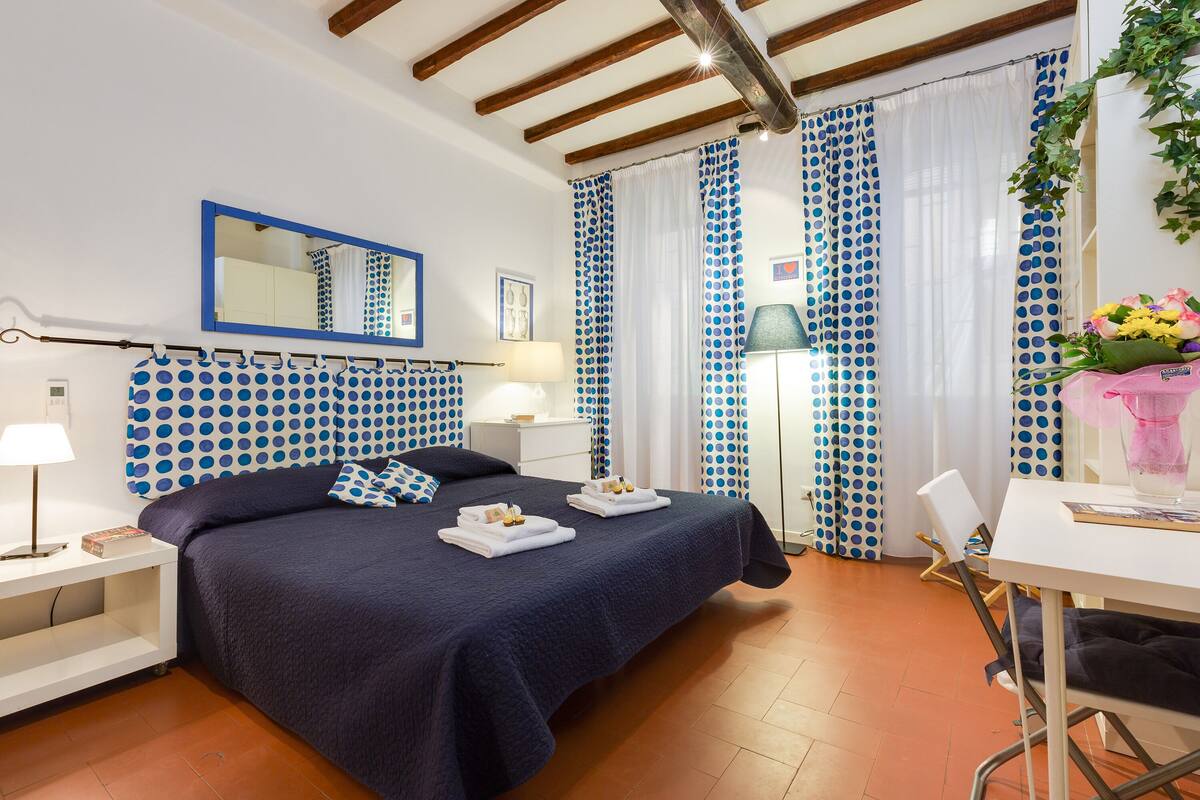 A bedroom with a bed, bedside tables, a desk, and curtains.