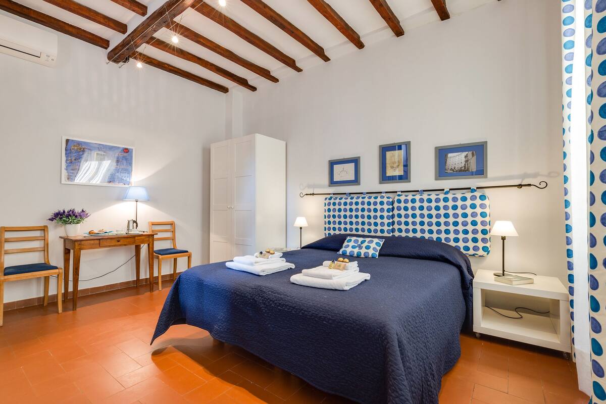 A bedroom with a bed, two chairs, a desk, and a wardrobe.