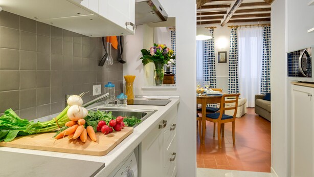 Une cuisine moderne avec une planche à découper en bois, des légumes frais et un coin repas comprenant une table et des chaises.