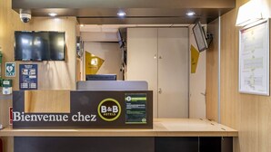 A reception desk with a 'Bienvenue chez B&B Hotels' sign, a digital screen, and a security camera. - B&B Hotel Bordeaux Merignac Hotel De Ville (Merignac)