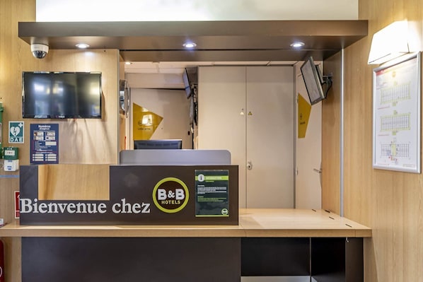 A reception desk with a 'Bienvenue chez B&B Hotels' sign, a digital screen, and a security camera. - B&B Hotel Bordeaux Merignac Hotel De Ville (Merignac)