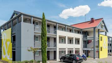 A multi-story hotel with a parking area, a car, and a motorcycle.