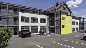 A multi-story hotel with a prominent yellow and white facade, a covered outdoor area, and a parking lot with cars. - B&B Hotel Bordeaux Merignac Hotel De Ville (Merignac)