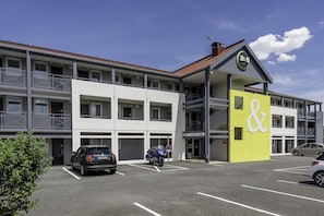 Um hotel com vários andares, fachada amarela e branca marcante, área externa coberta e estacionamento com carros.