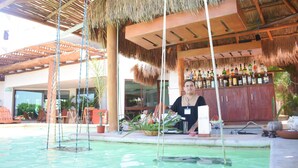 A pool area with a bar and seating under a thatched roof. - Hotel Rio Lagartos (Río Lagartos)