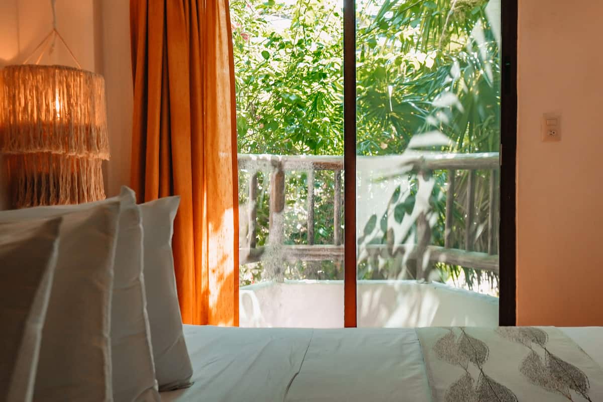 A bedroom with a bed, curtains, and a view of greenery outside.