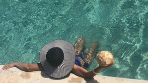 A person in a swimming pool with a striped hat, holding a coconut. - Hotel Rio Lagartos (Río Lagartos)