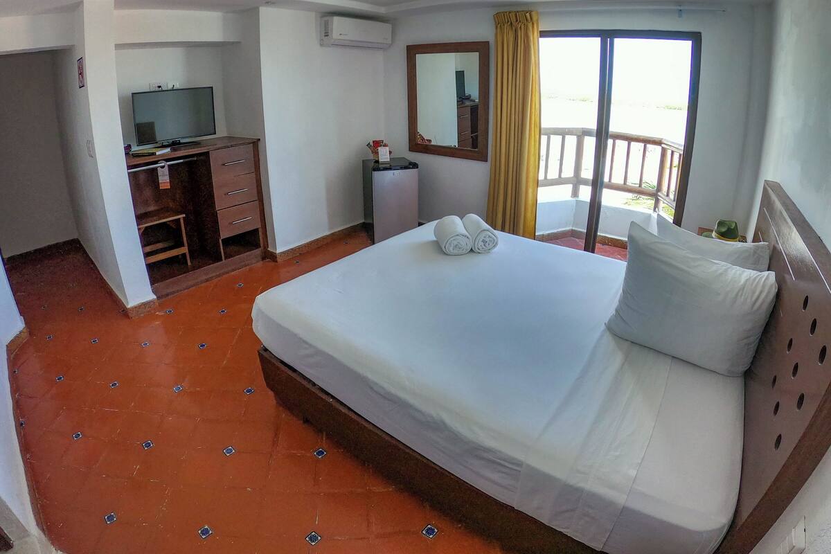 A hotel room with a bed, a desk, a television, and a balcony with a yellow curtain.