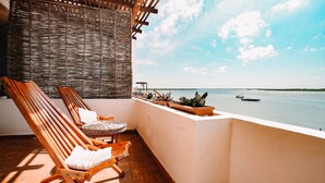 A balcony with two wooden lounge chairs, a wicker wall, and potted plants. - Hotel Rio Lagartos (Río Lagartos)