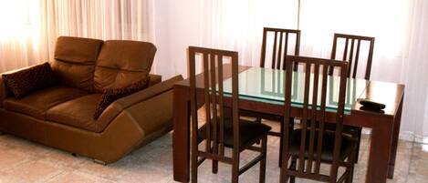 Una sala de estar con un sofá marrón, una mesa de comedor con superficie de vidrio y sillas de madera.