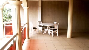 A dining area with a table and four chairs, surrounded by columns and a balcony with a railing.