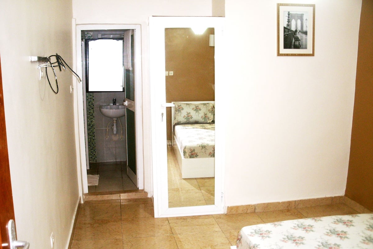 Ein Schlafzimmer mit Bett, ein Badezimmer mit Waschbecken und eine Tür zu einem anderen Raum.