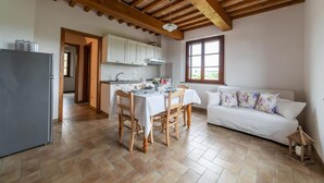 A spacious kitchen with wooden beams, a dining area with a table set for four, and a white sofa with floral cushions. - Il Mandorlo b&b (Florence)
