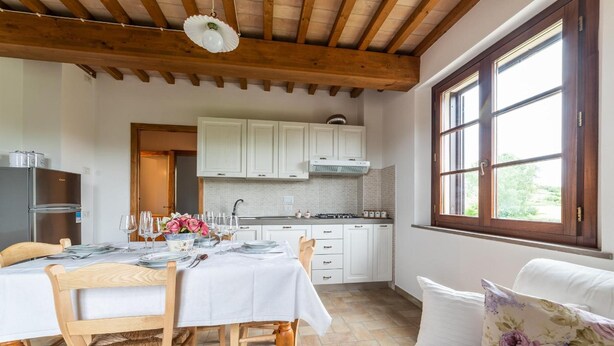 A dining area with a table set for four, wooden chairs, a white tablecloth, and a window with a view of greenery. - Il Mandorlo b&b (Florence)