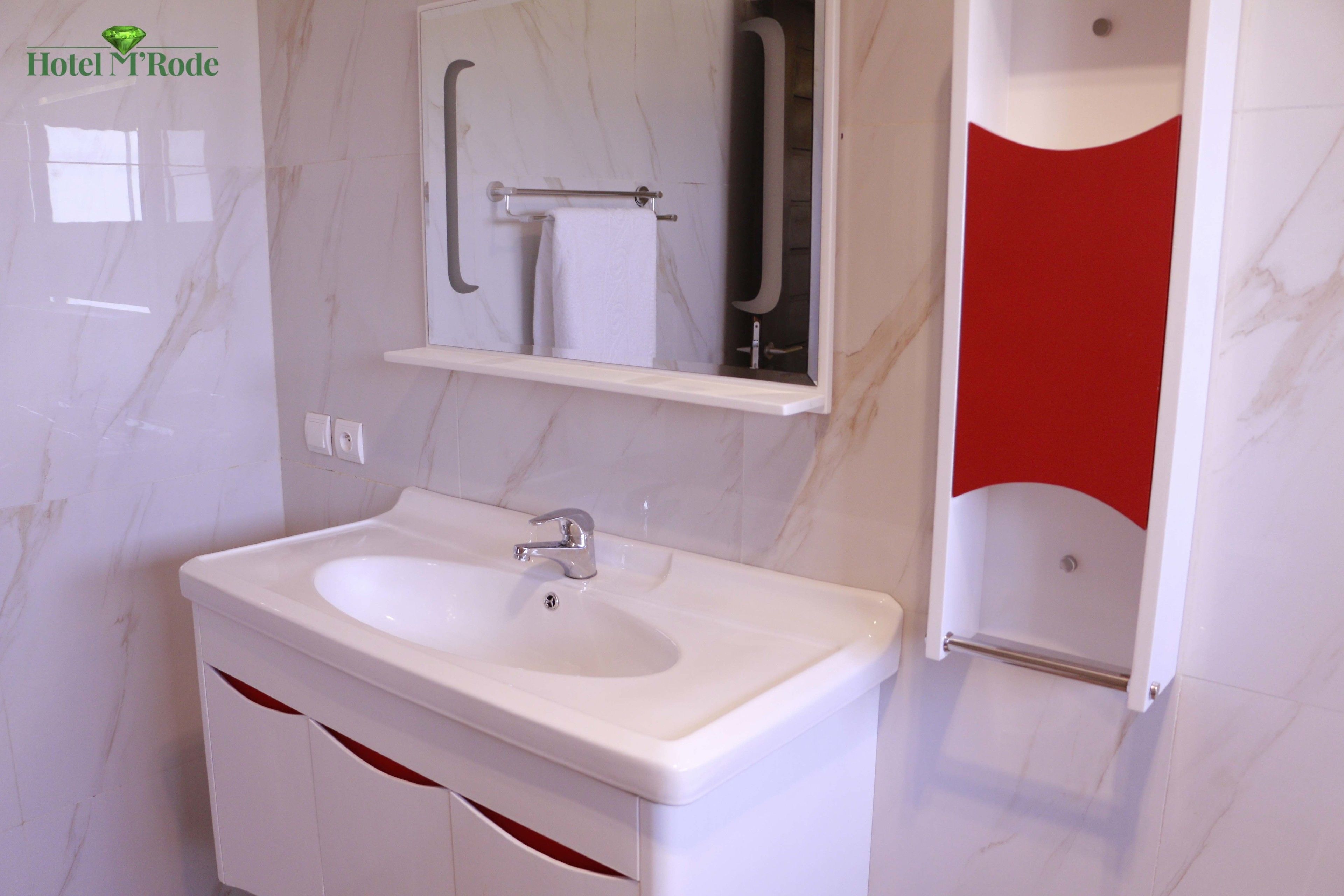 A modern bathroom with a white sink, a mirror, and a red accent wall.
