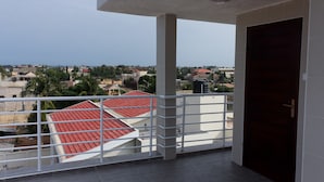 Ein Balkon mit Blick auf eine Wohngegend, ein Gebäude mit rotem Dach und eine geschlossene Tür.