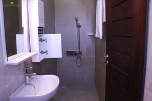 A bathroom with a white sink, a mirror, a shower, and a wooden door. - Appart MRode Baguida (Lomé)