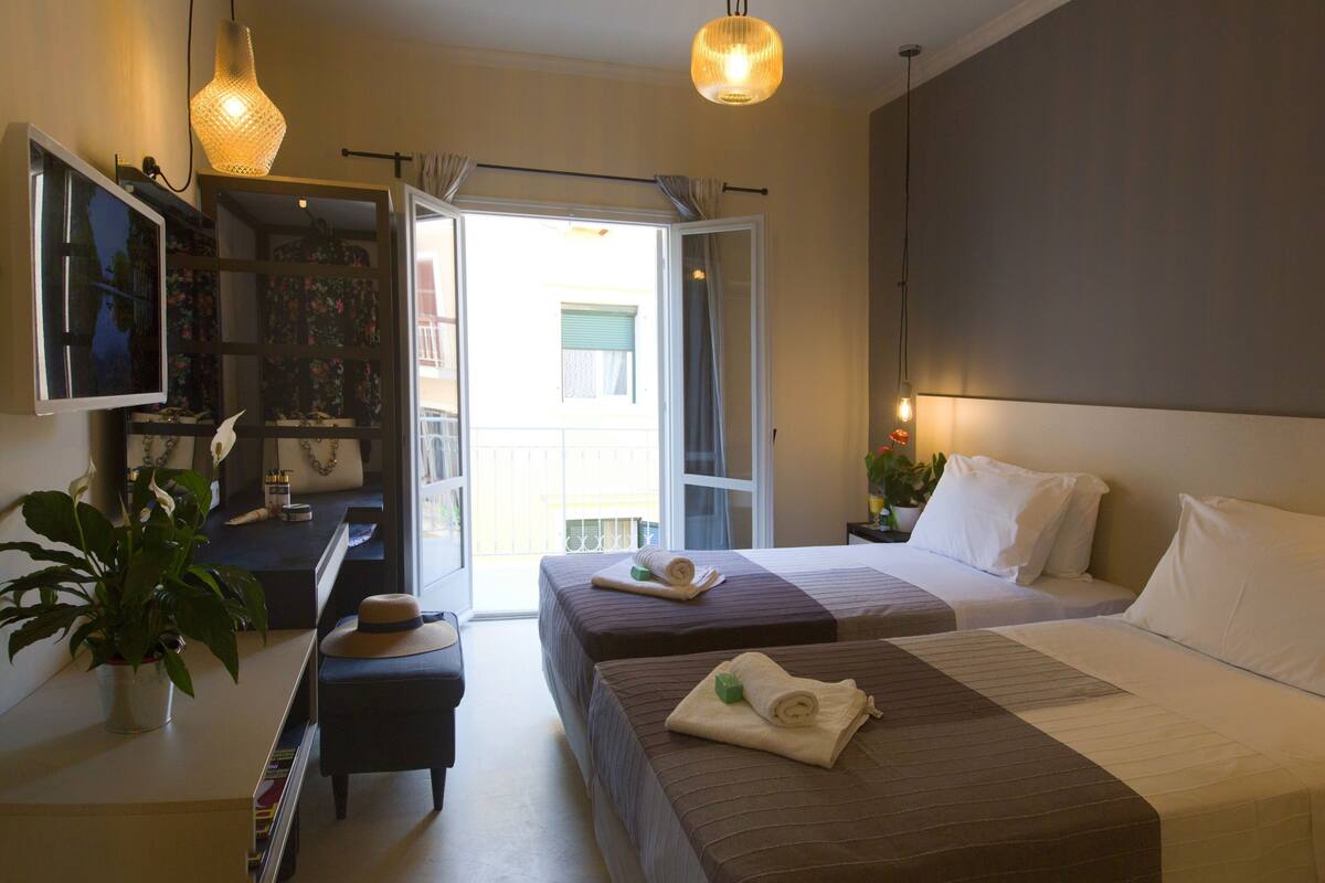 A hotel room with two beds, a desk, a television, and a large window.