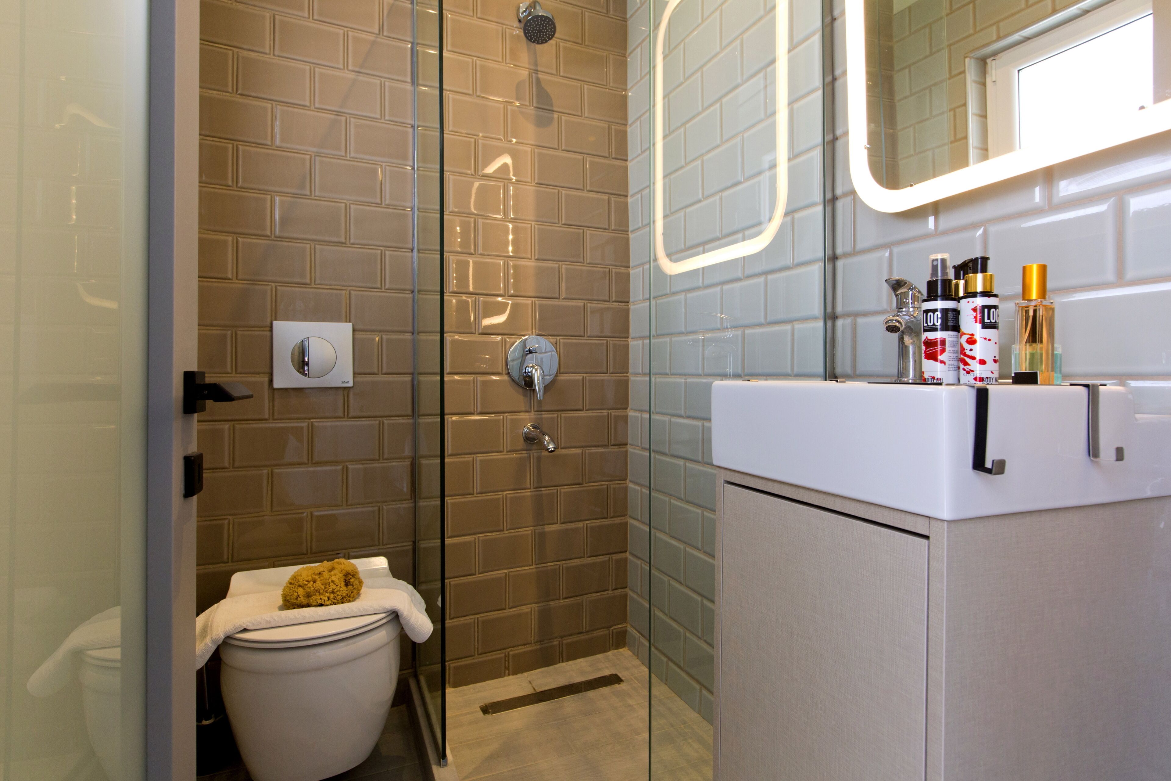 Un baño moderno con cabina de ducha de vidrio, inodoro con toalla y lavamanos con artículos de aseo.