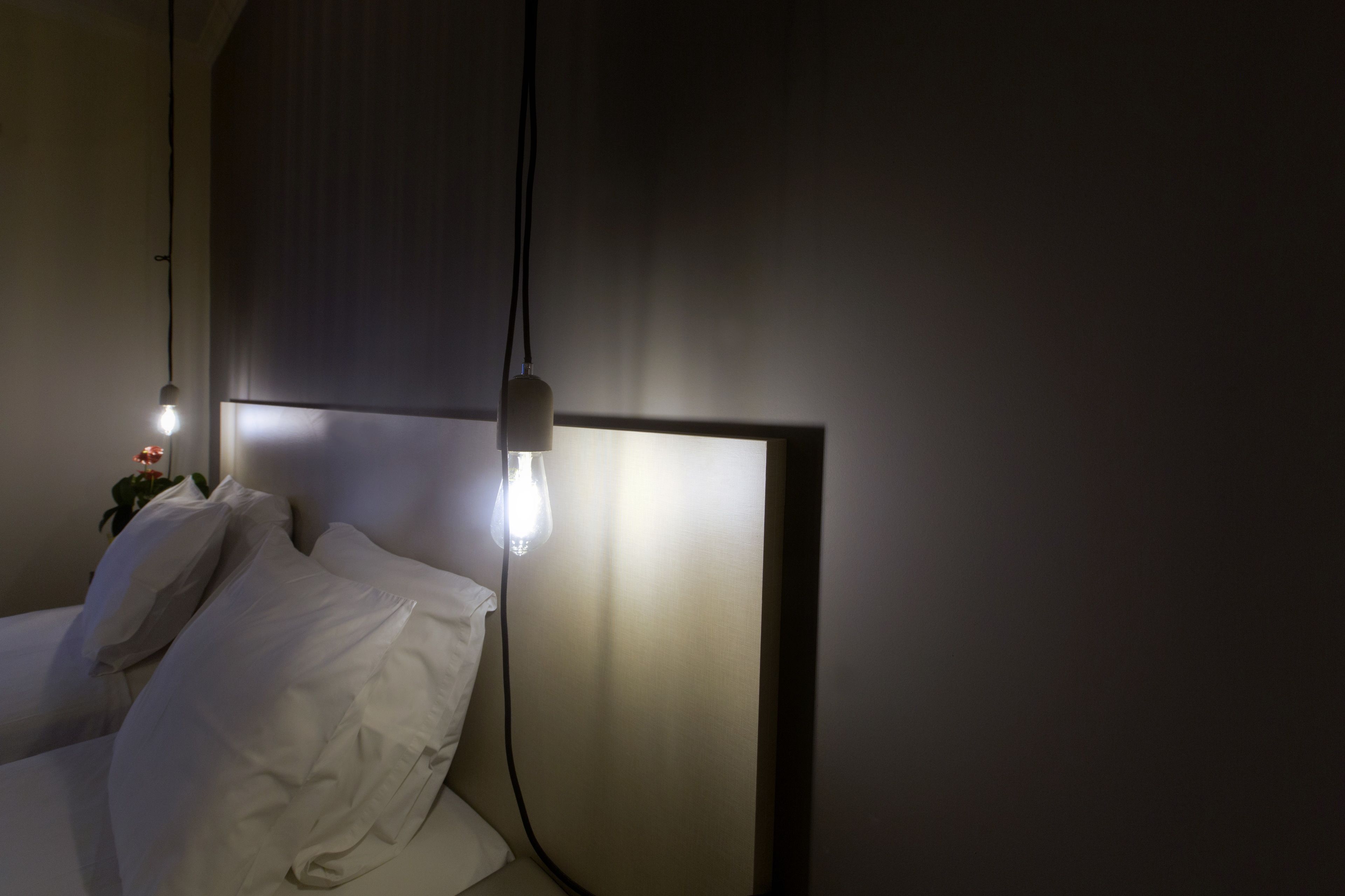 A dimly lit room with a bed, a bedside lamp, and a wall-mounted light fixture.