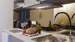 A modern kitchen with a stainless steel sink, a built-in oven, and a range hood. There are various kitchen items on the counter, including a loaf of bread, tomatoes, and bottles. - ANNUNZIATA URBAN SUITES by LOC HOSPITALITY (Corfu)