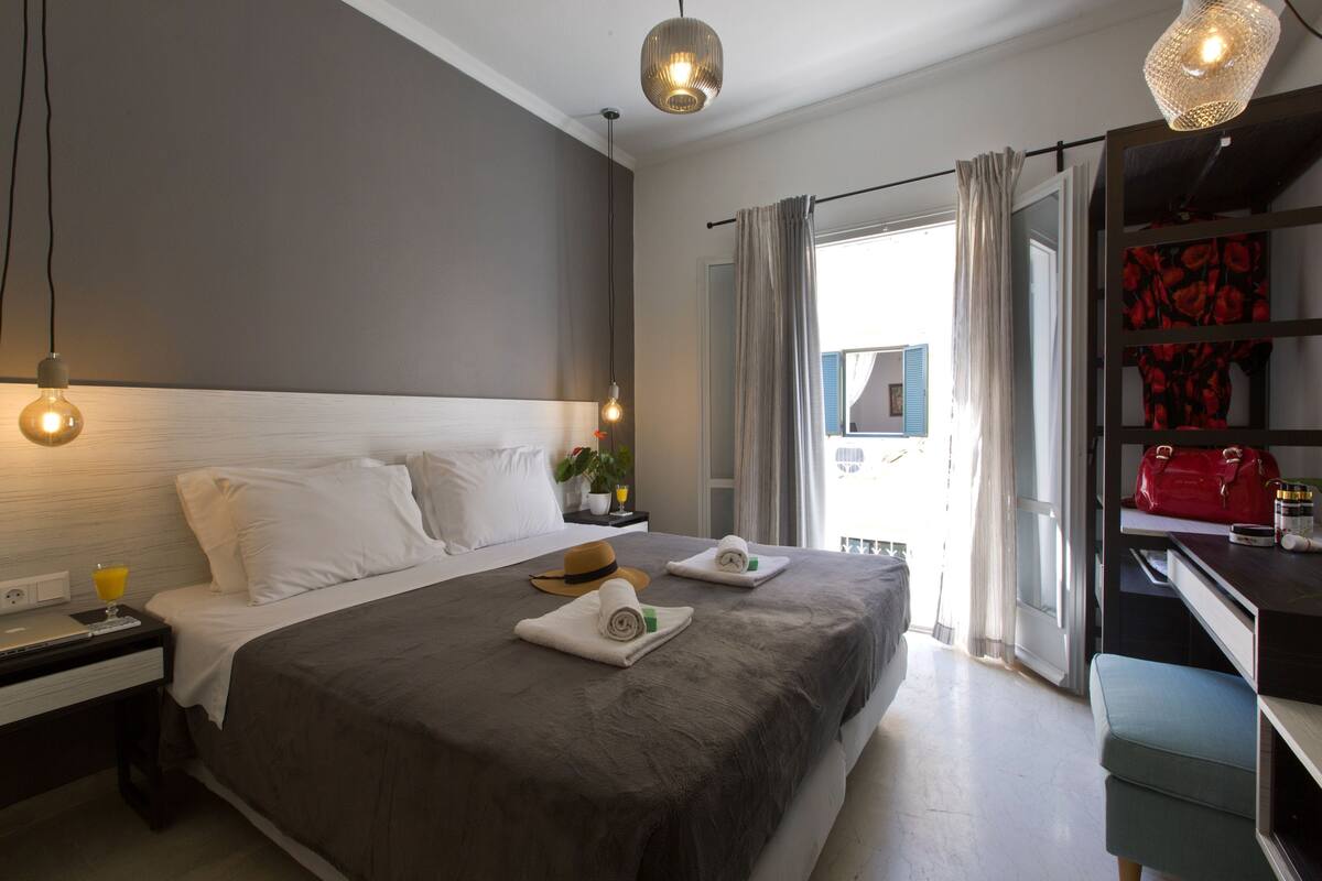 A neatly made bed with white linens, a bedside table with a lamp, and a red handbag on a shelf.