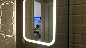 A bathroom with a mirror, a potted plant, and a view of a cityscape through an open door. - ANNUNZIATA URBAN SUITES by LOC HOSPITALITY (Corfu)