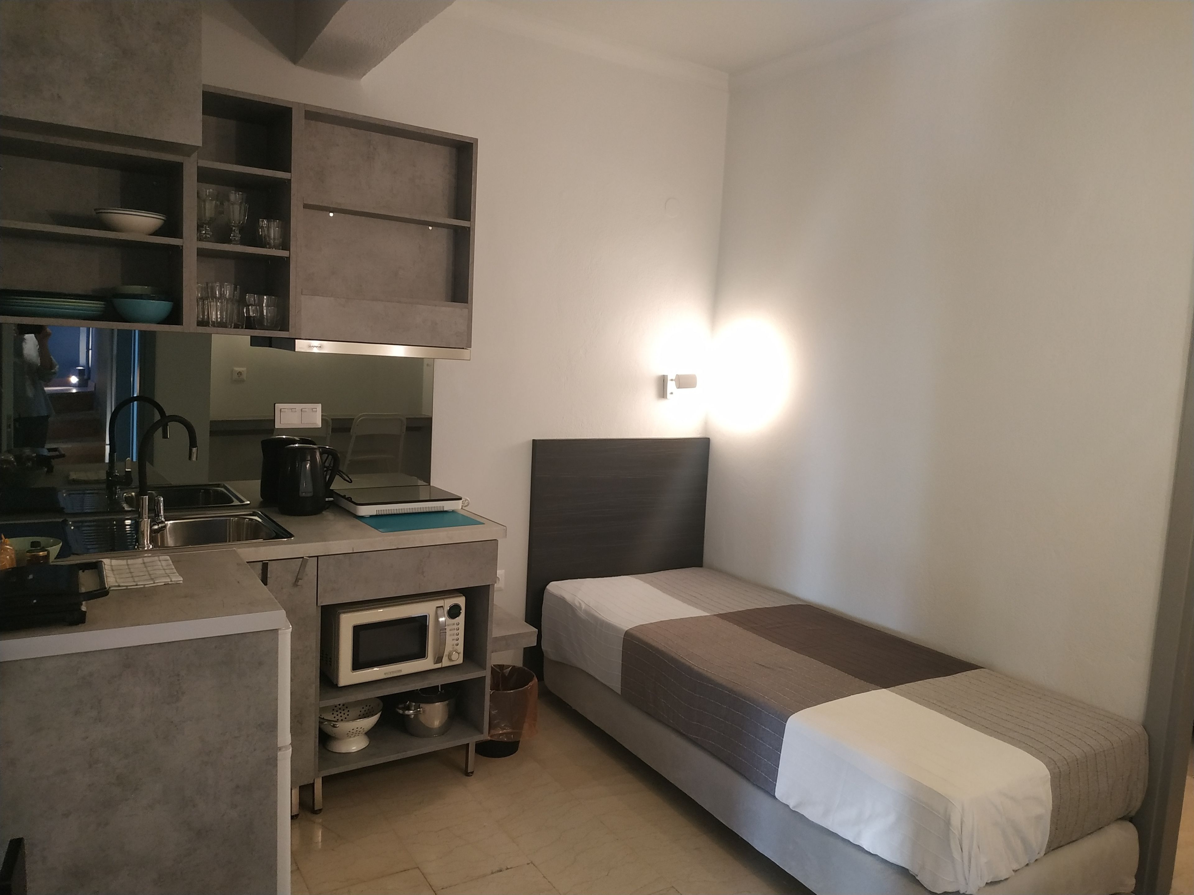 Habitación de hotel compacta con kitchenette, una cama y una pequeña zona de escritorio.