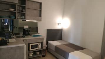 Habitación de hotel compacta con kitchenette, una cama y una pequeña zona de escritorio.