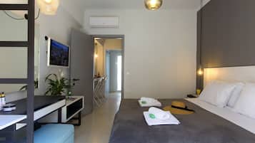 A modern hotel room with a bed, bedside table, and a desk with a chair. There is a television mounted on the wall, a potted plant, and a window.