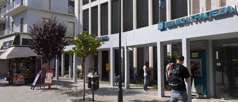 A bank with a modern facade, outdoor seating, and a tree in front.