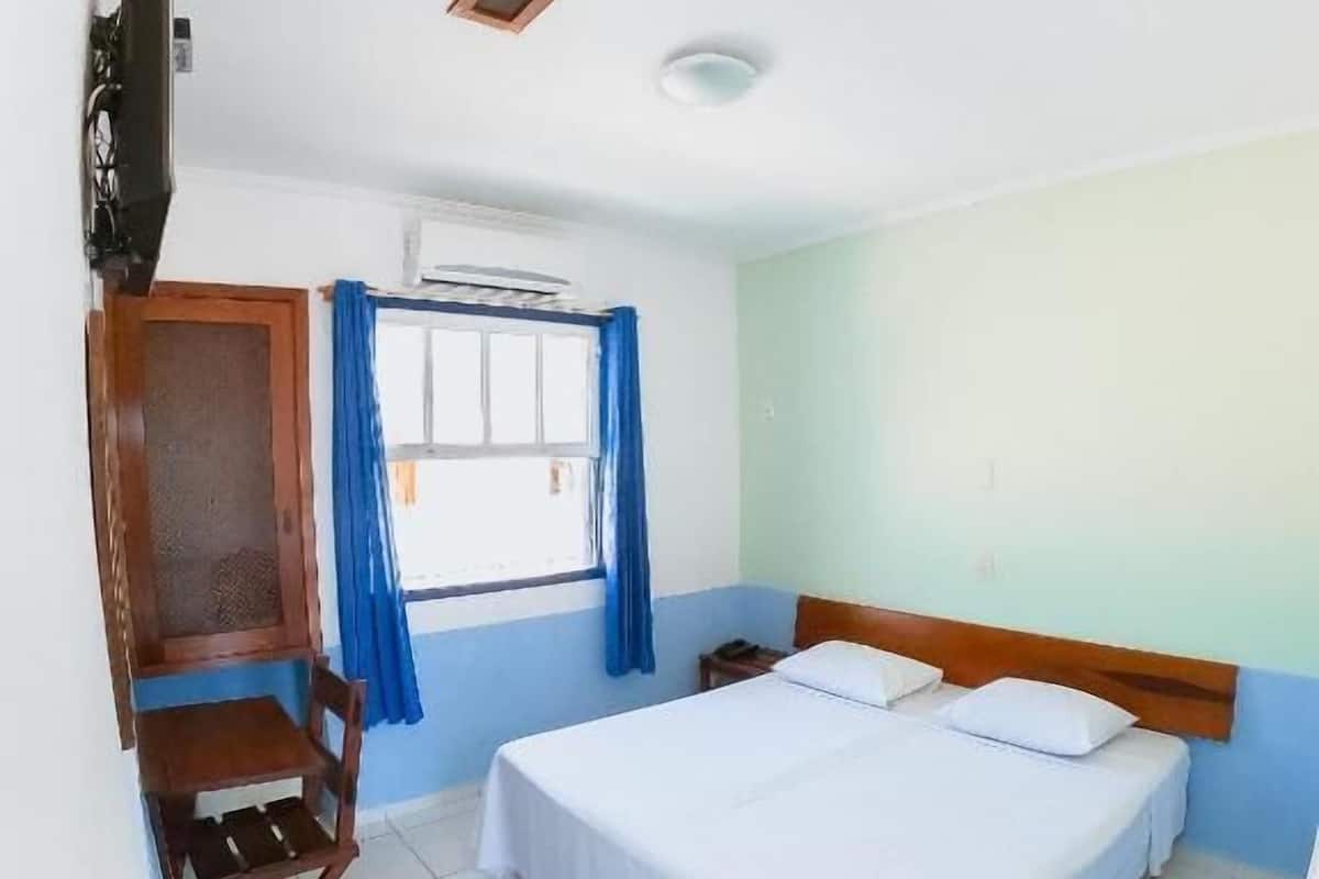 A room with a bed, a desk, a chair, a TV, and a window with curtains.