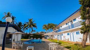 A hotel with a swimming pool, outdoor seating, and palm trees.