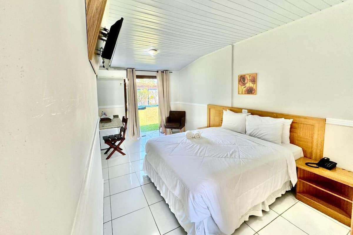A hotel room with a large bed, a wooden headboard, a bedside table with a phone, a chair, and a TV mounted on the wall.