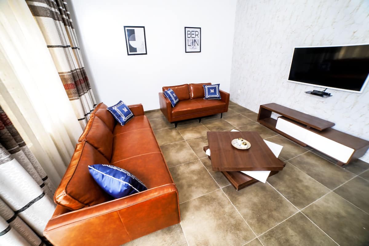 A living room with a brown leather sofa, a wooden coffee table, and a TV mounted on the wall.