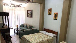 Une petite pièce agréable et confortable, avec un lit, un canapé, un bureau et une chaise. Il y a deux tableaux au mur et une fenêtre avec des rideaux.