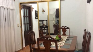 Un coin repas avec une cuisinière à gaz, des chaises en bois, une table et un réfrigérateur à l’arrière-plan.