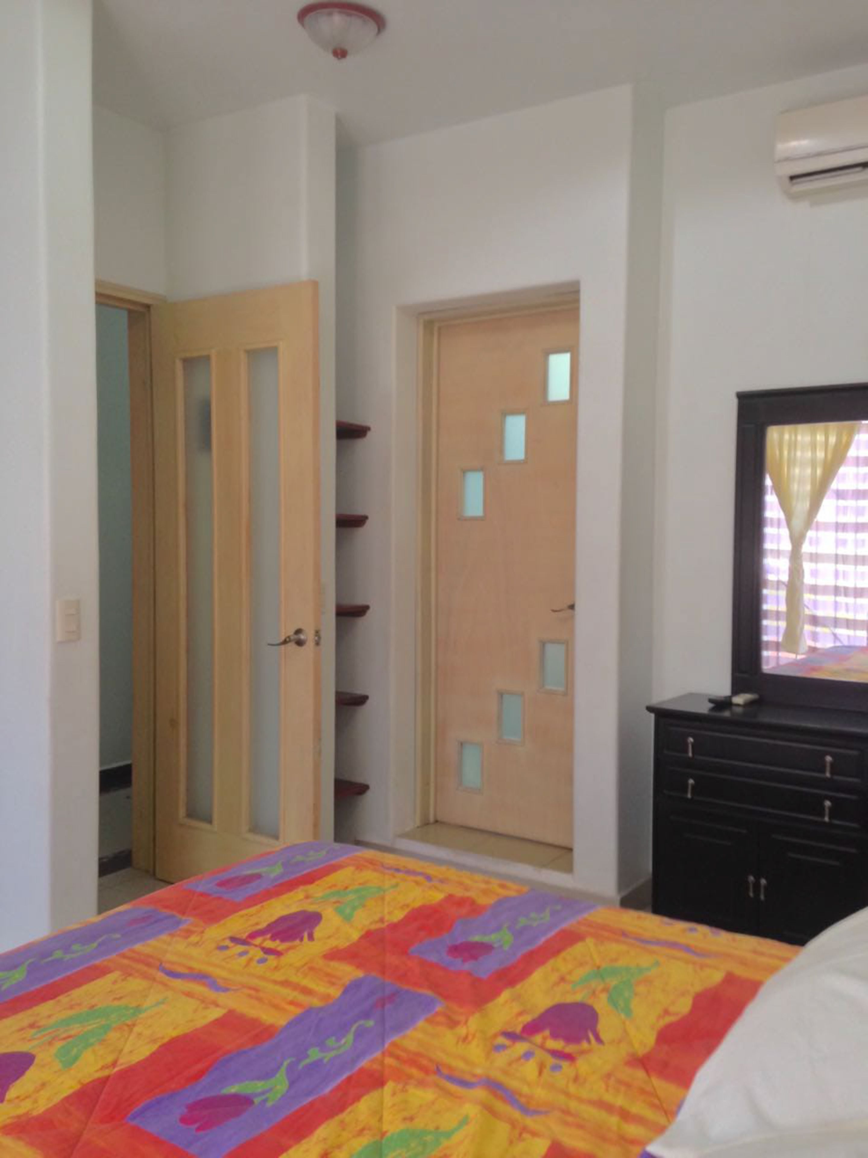 A bedroom with a bed, a dresser, a door with a mirror, and a ceiling light.