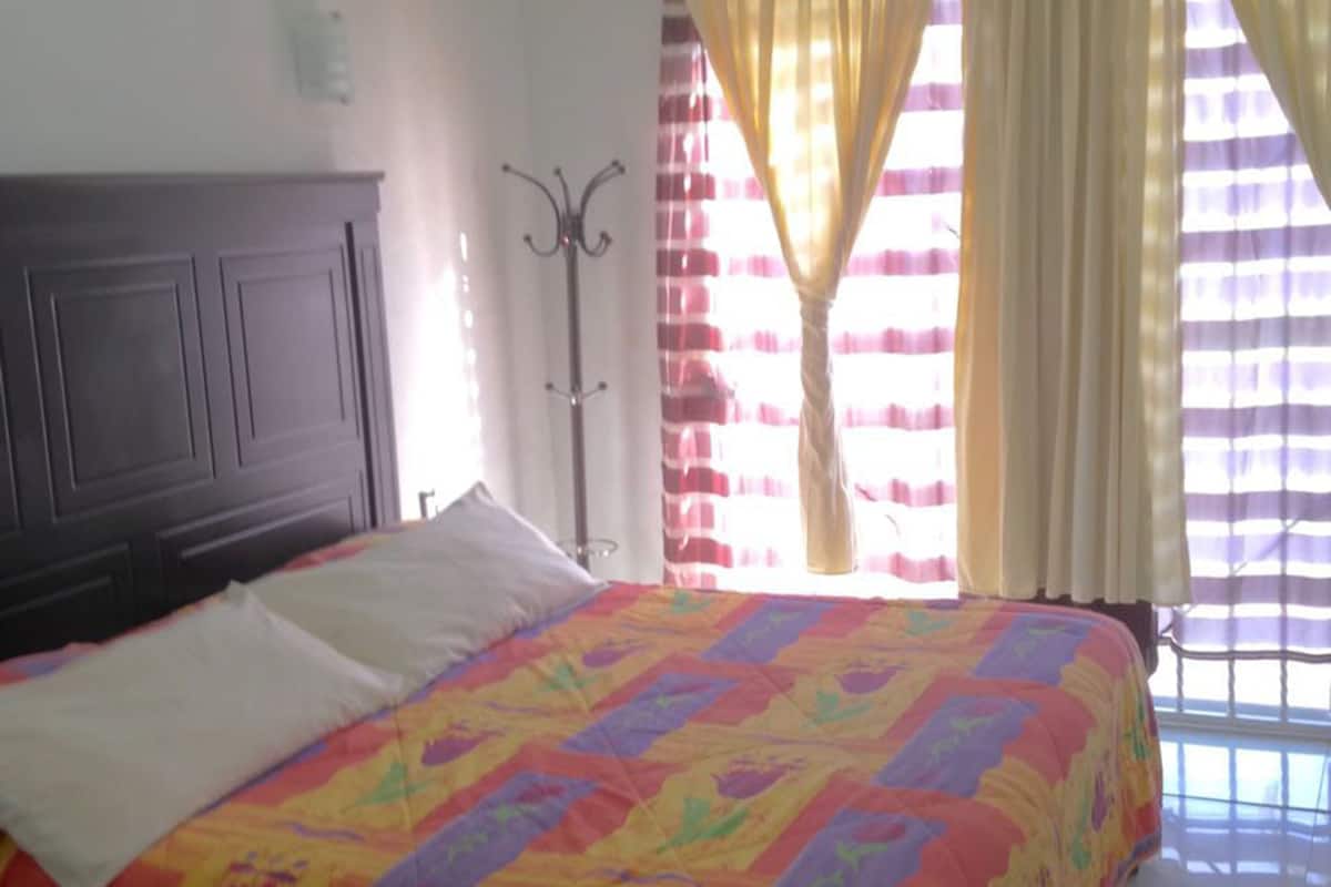 Une chambre à coucher avec un grand lit, une tête de lit sombre et une fenêtre avec des rideaux.