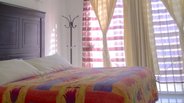 Une chambre à coucher avec un lit, un ventilateur de plafond, un porte-manteau et des rideaux.